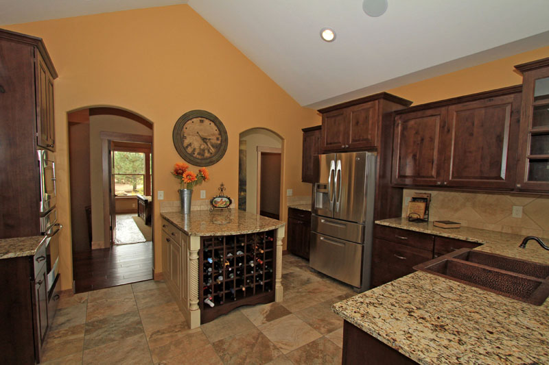 Kitchen with dark wood cabinetry, granite countertops, tile flooring, stainless steel appliances, and a built-in wine rack island.