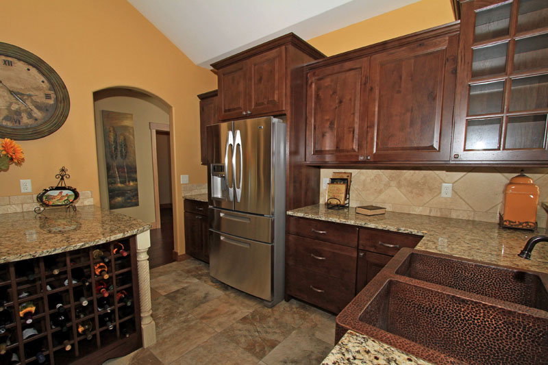 Close-up view of a custom kitchen featuring dark wood cabinets, granite countertops, a hammered copper sink, and a stainless steel refrigerator.