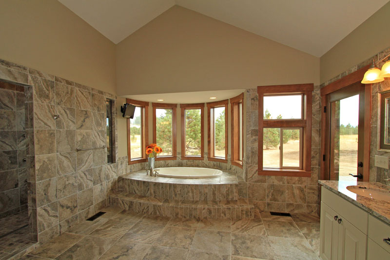 Primary bathroom with neutral tile walls, a walk-in tile shower, and a platform bathtub set inside a bay of wood-trimmed windows.